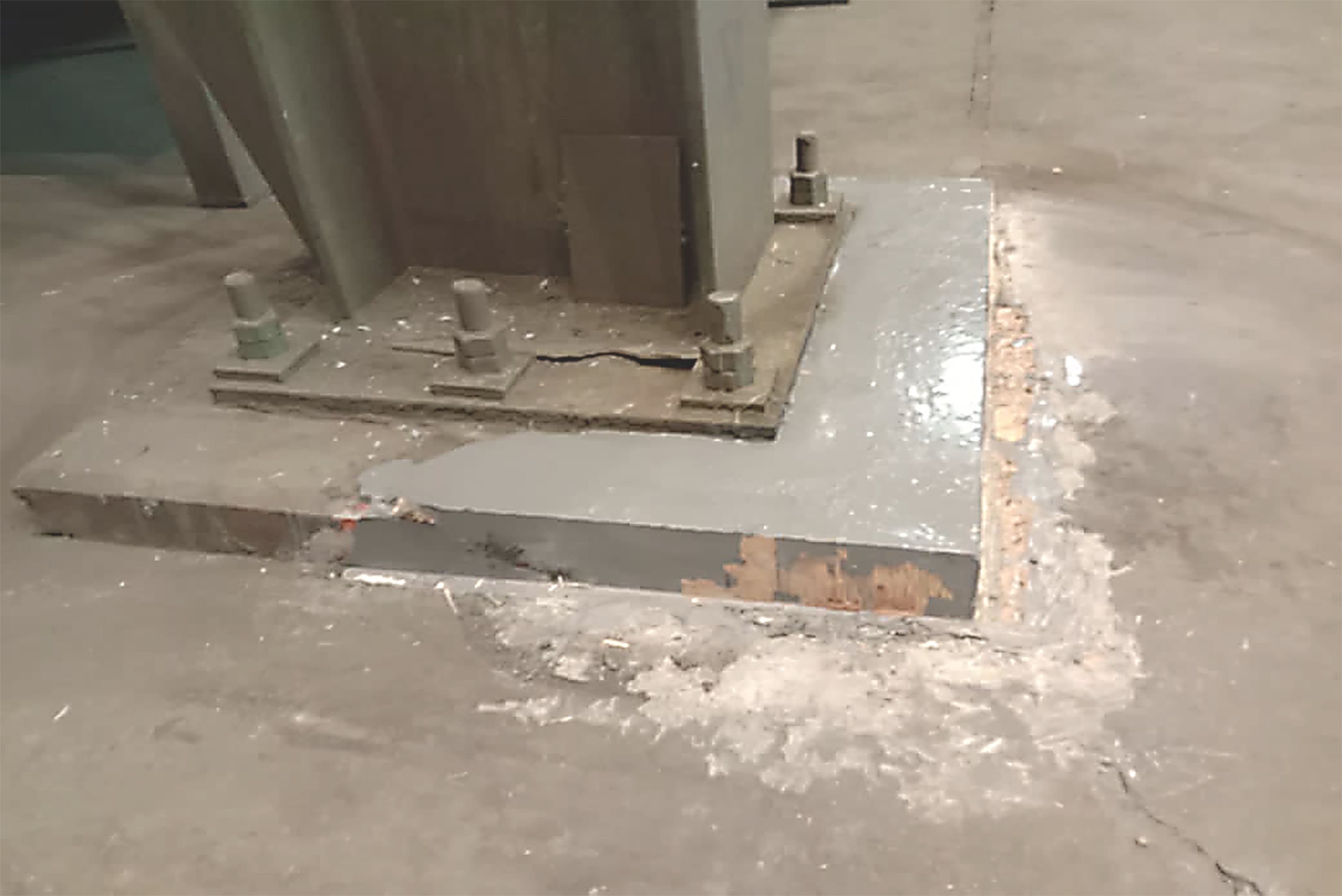 Close-up view of a stable steel support column with a bolted base plate mounted on a concrete foundation, where the edges and surface area have been finished with a glossy, gray protective coating.