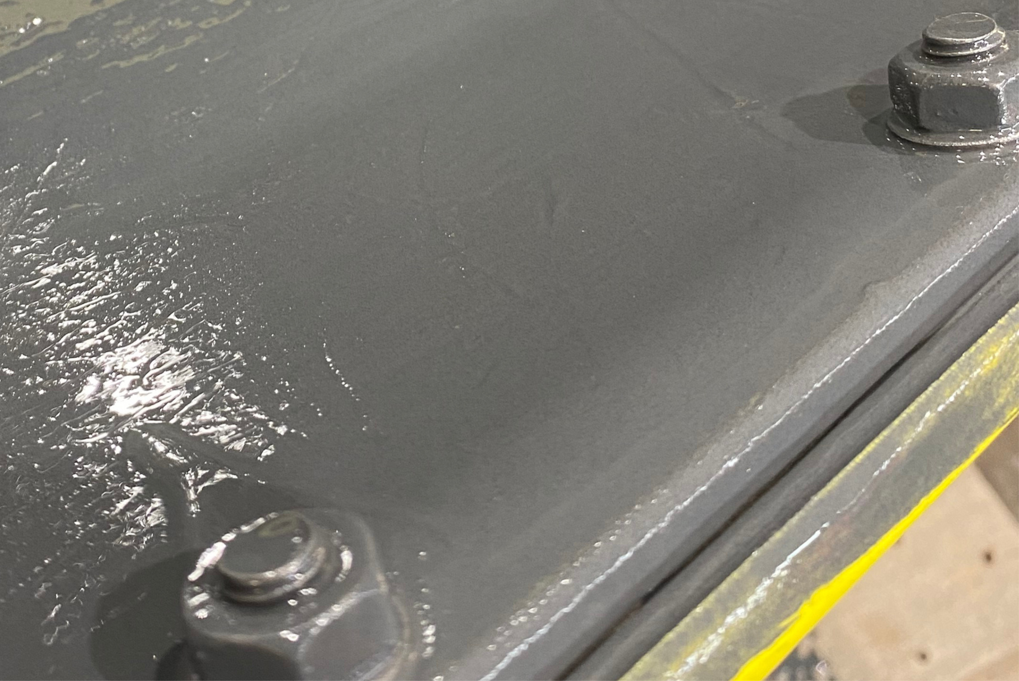 Close-up view of a flat steel plate with two hex bolts fully sealed and covered with a smooth, grey protective coating.