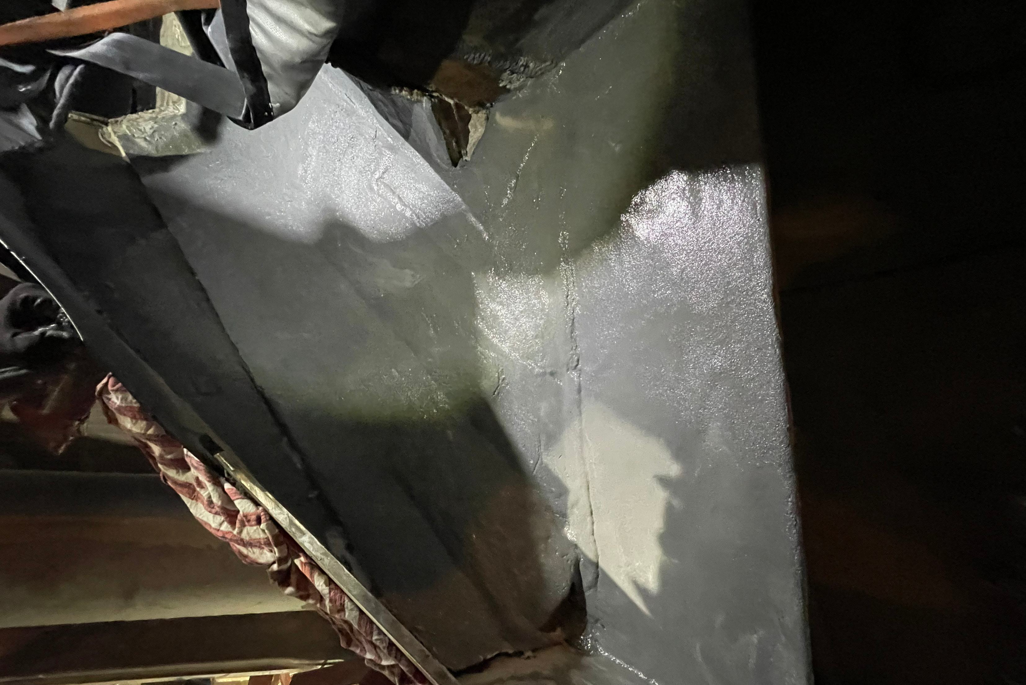 An interior view showing a dark grey, smooth protective coating applied across the corner seams and walls of an industrial container or chute, illuminated by a task light.