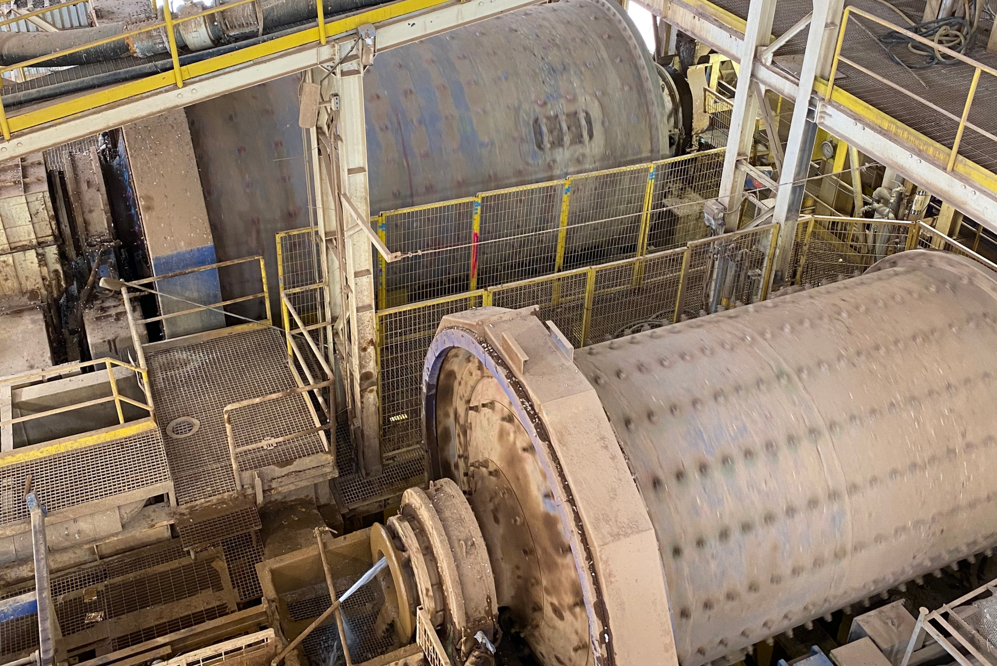 An elevated, high-angle view of large cylindrical grinding ball mills and surrounding steel catwalks inside an industrial processing facility.