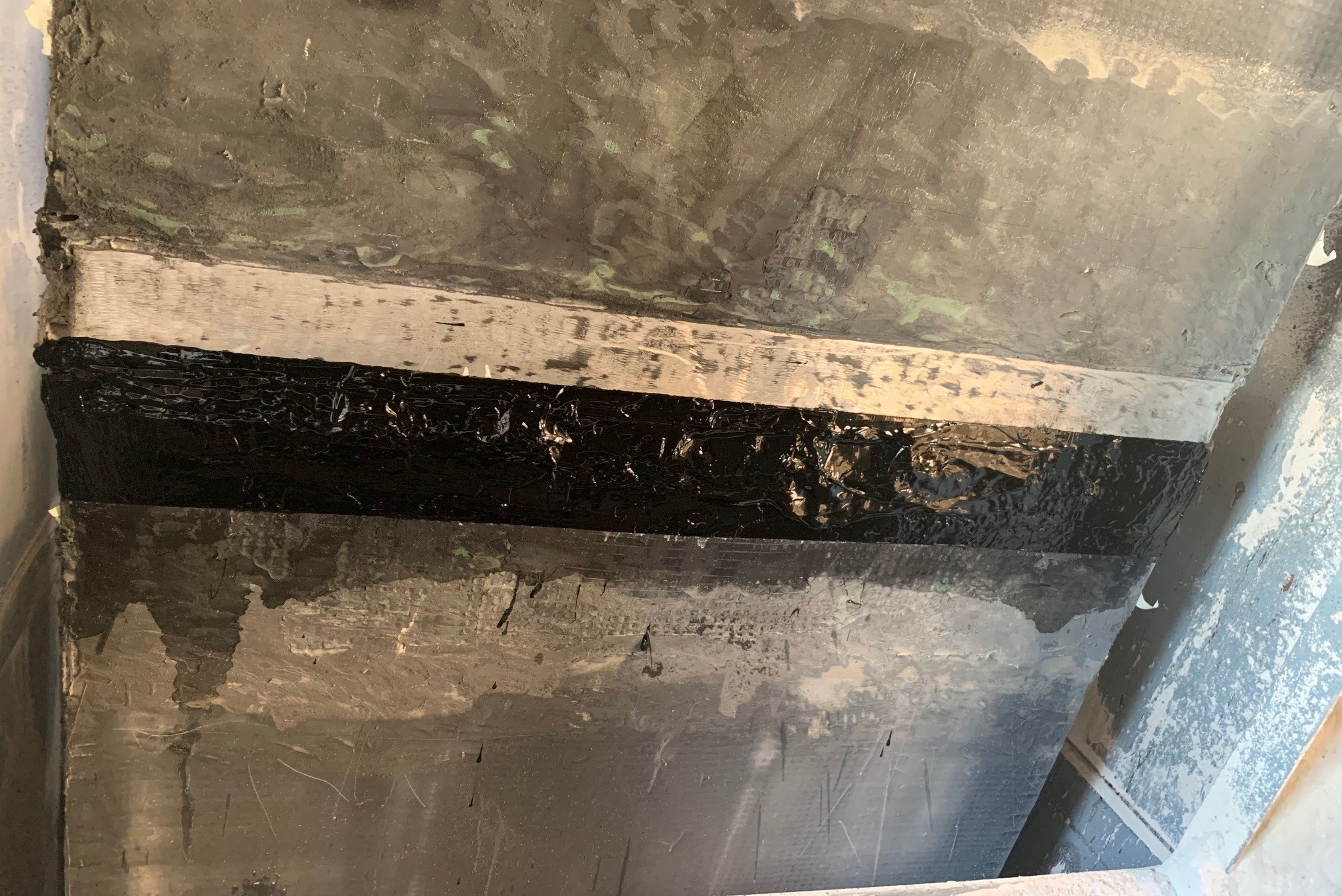 Detailed view of a concrete structure joint that has been sealed with a broad band of black protective compound over a freshly prepared surface.