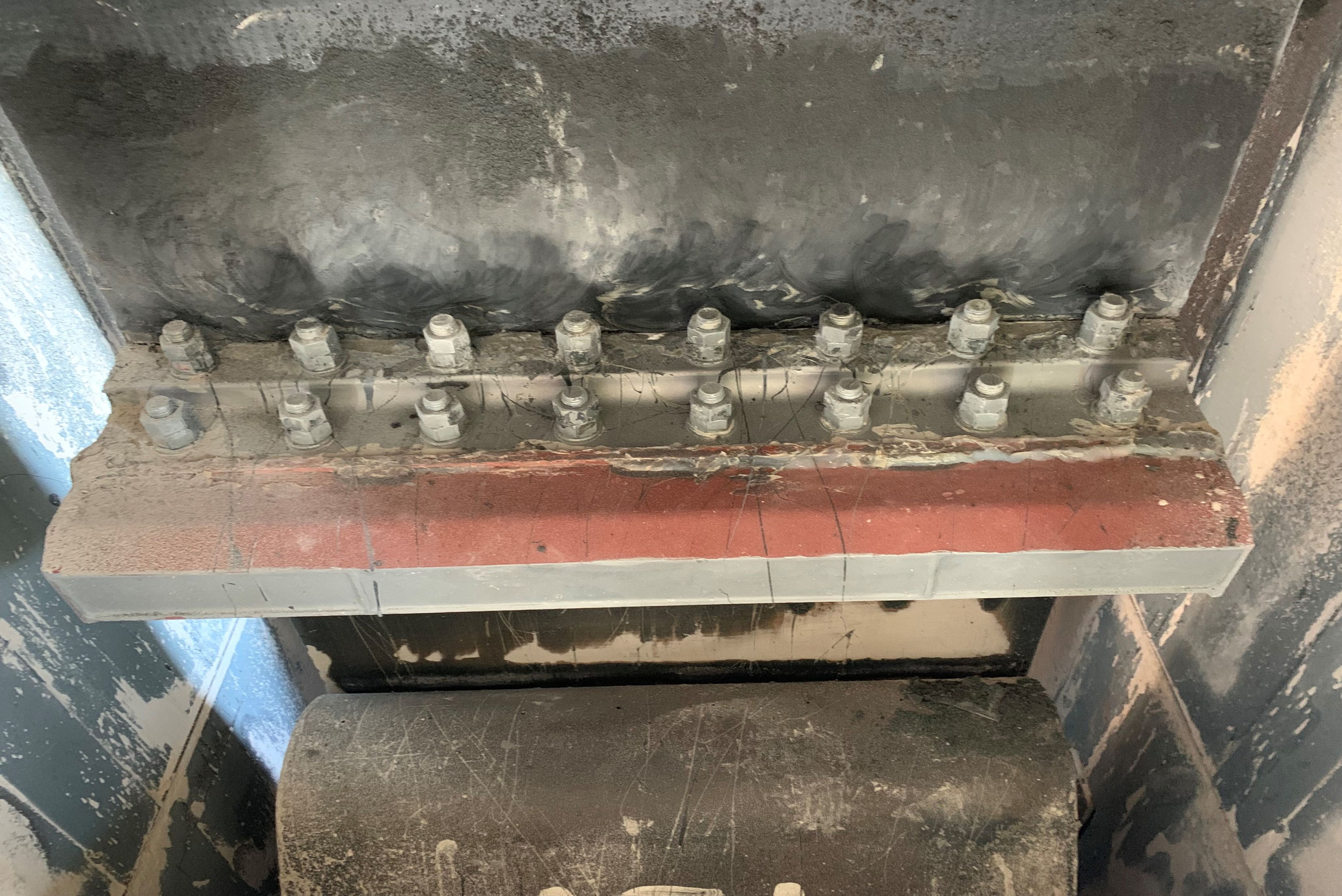 Detailed view of a heavy industrial steel structure featuring a double row of high-strength bolts along a flange beam, positioned directly above a large cylindrical steel roller.