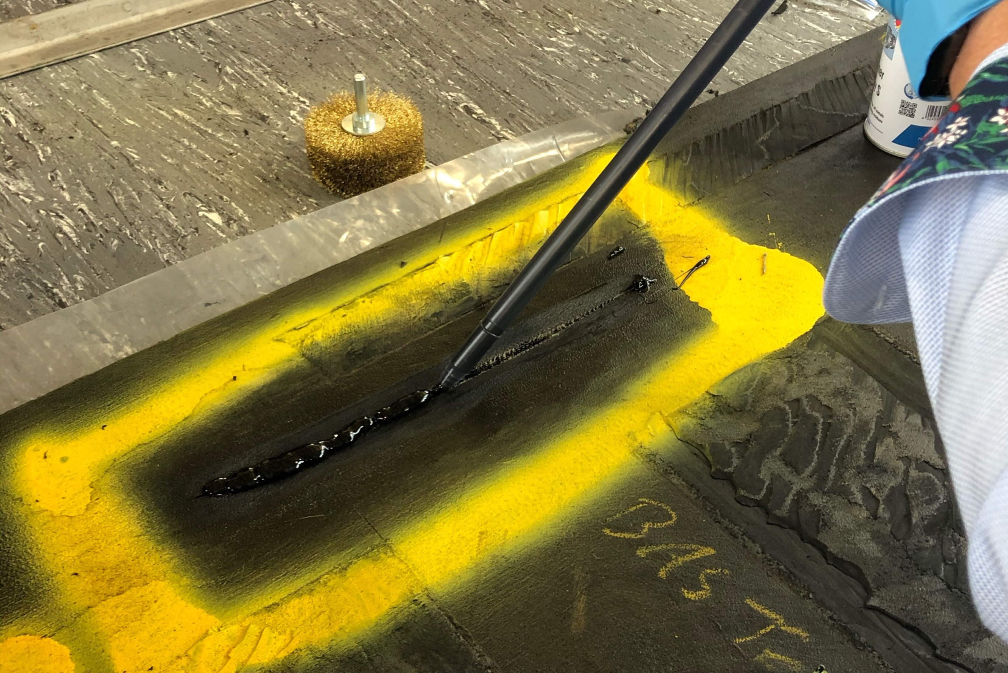 Close-up of a person applying a dark sealant or adhesive line onto a marked surface using a dispensing tool or nozzle.