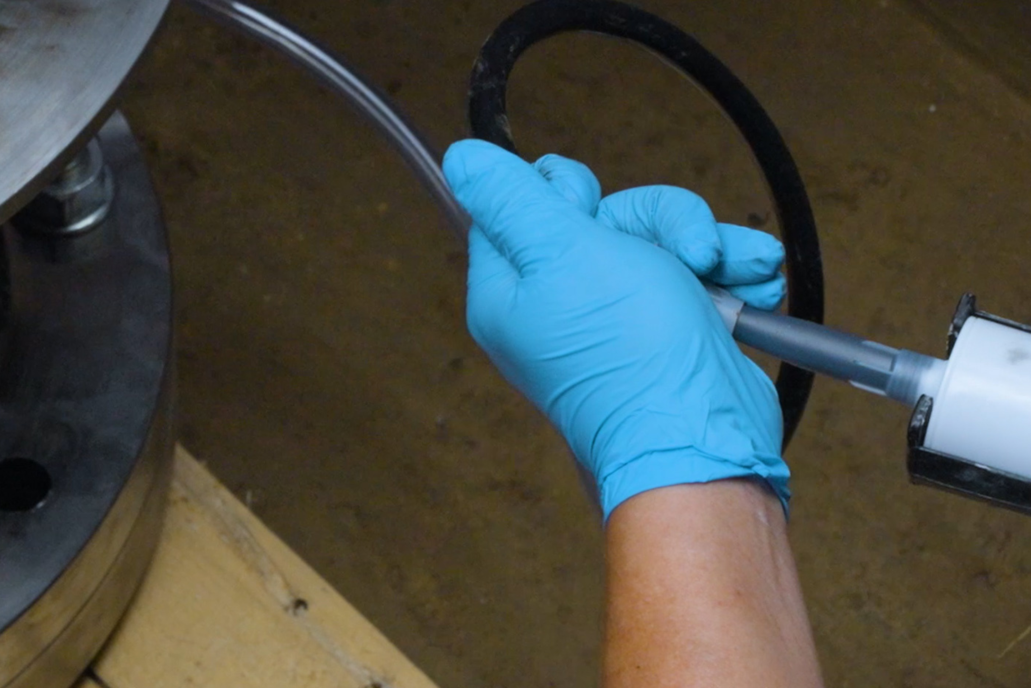 A gloved hand attaching a static mixer nozzle from a dispensing cartridge into a flexible transparent hose connected to a flange assembly.