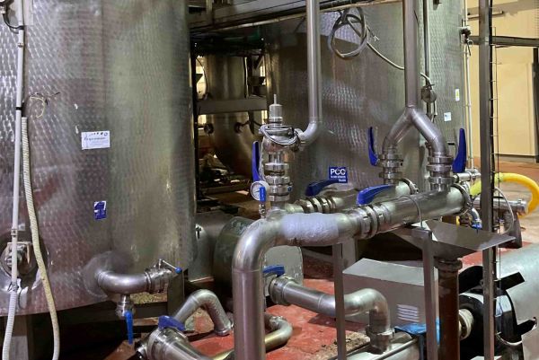 Stainless steel industrial tanks and pipes with blue-handled valves are installed in a processing facility.