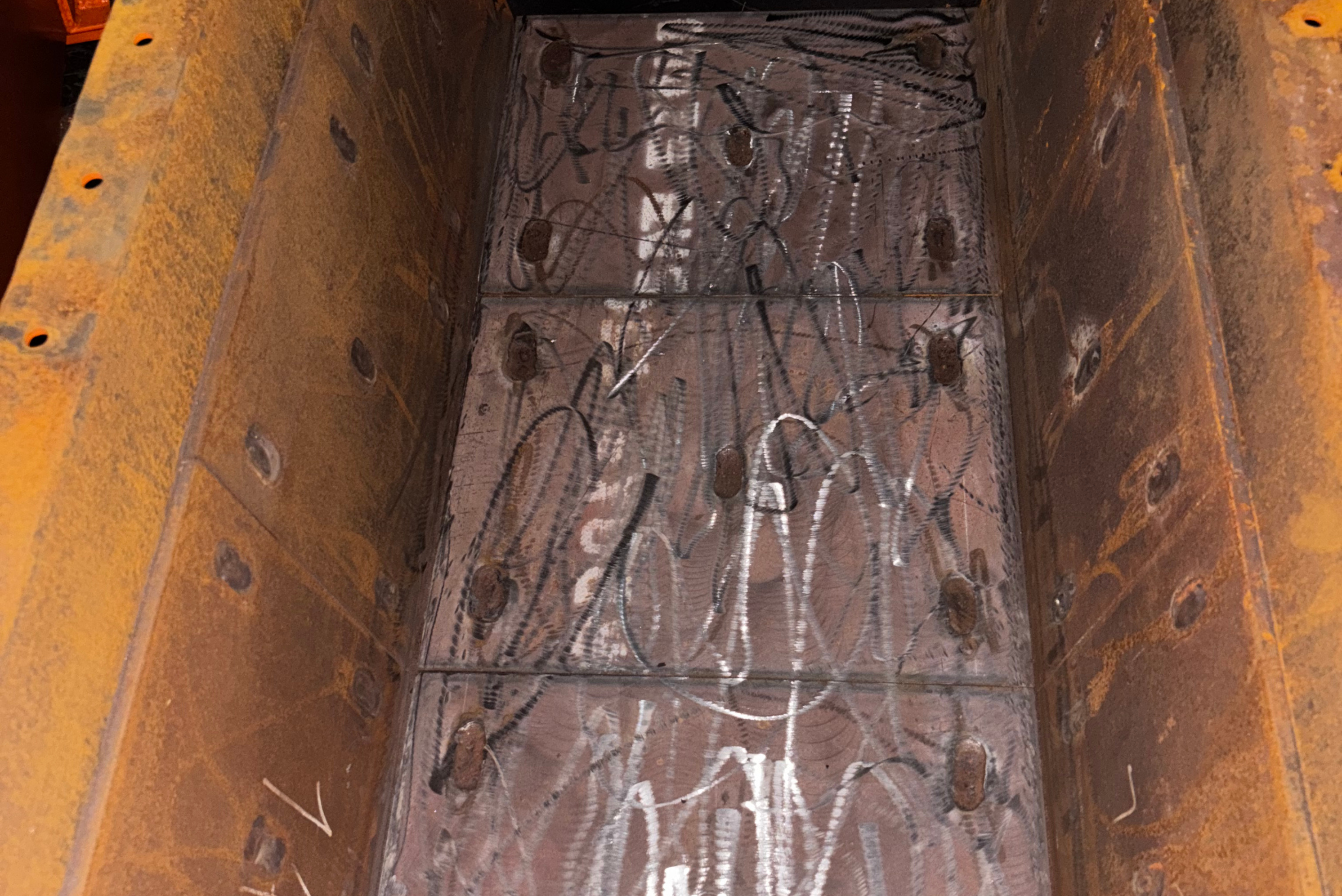 Interior view of a heavy-duty steel chute or hopper with ground and roughened metal plates prepared for wear protection lining.