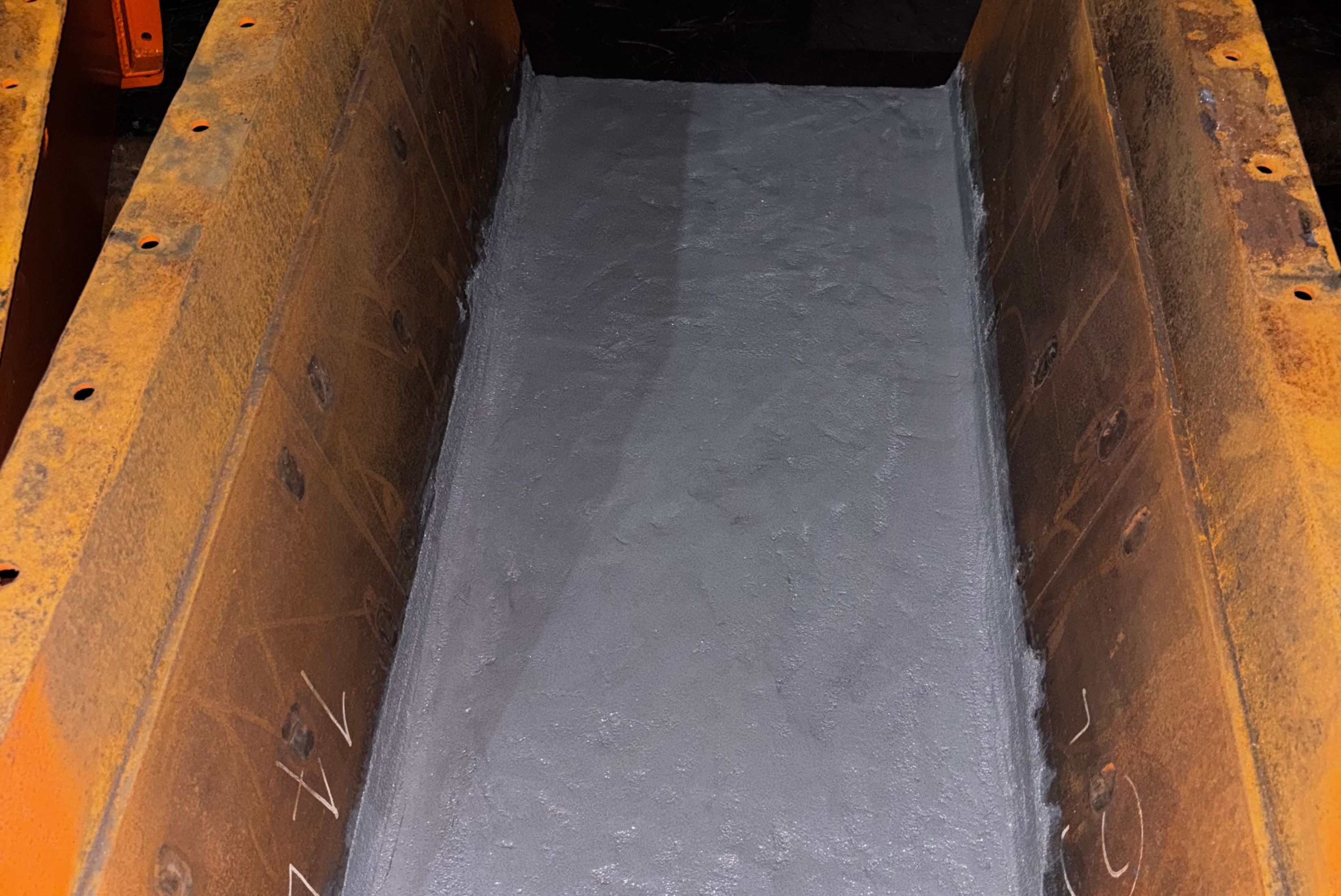 Interior view of an industrial steel chute featuring a smooth, freshly applied grey protective coating along its base